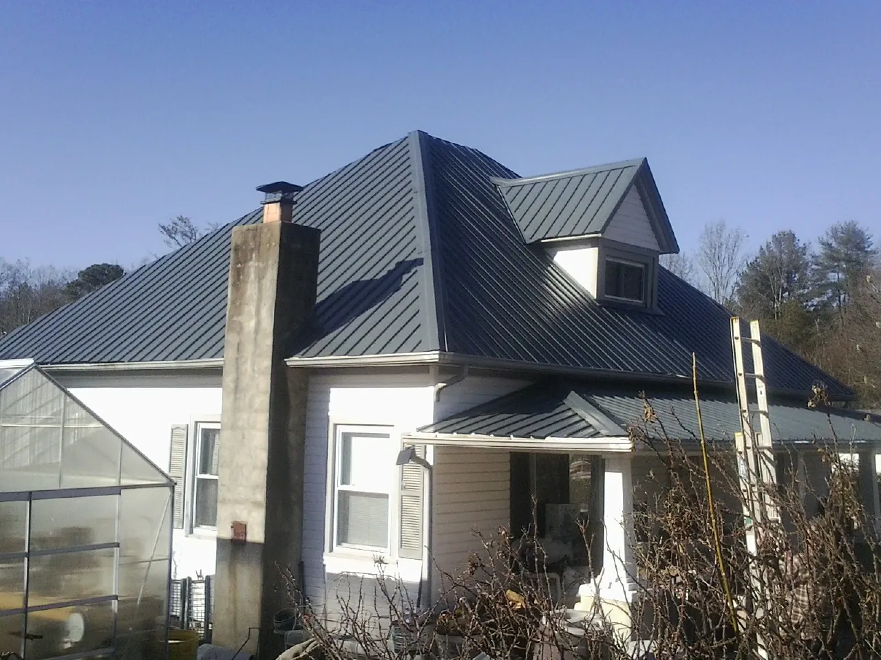 Dark blue standing seam metal roof on a white farmhouse with dormer — Slate & Tile Roof Repair by Roofing Brothers in Morgan City