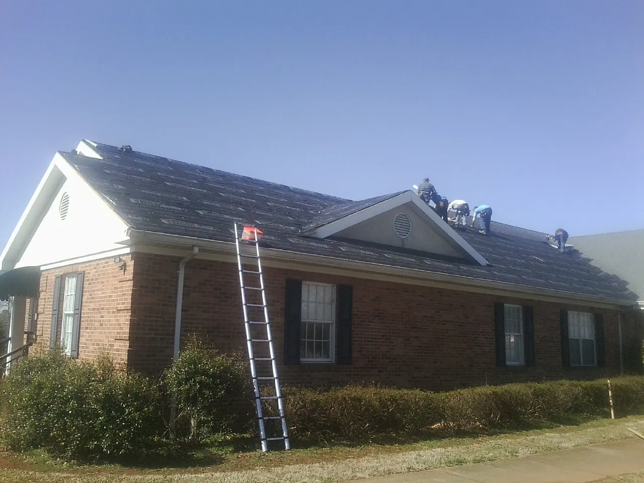 Crew tearing shingles off a brick ranch roof with a ladder set — Emergency Roof Repair work by our crew in Morgan City