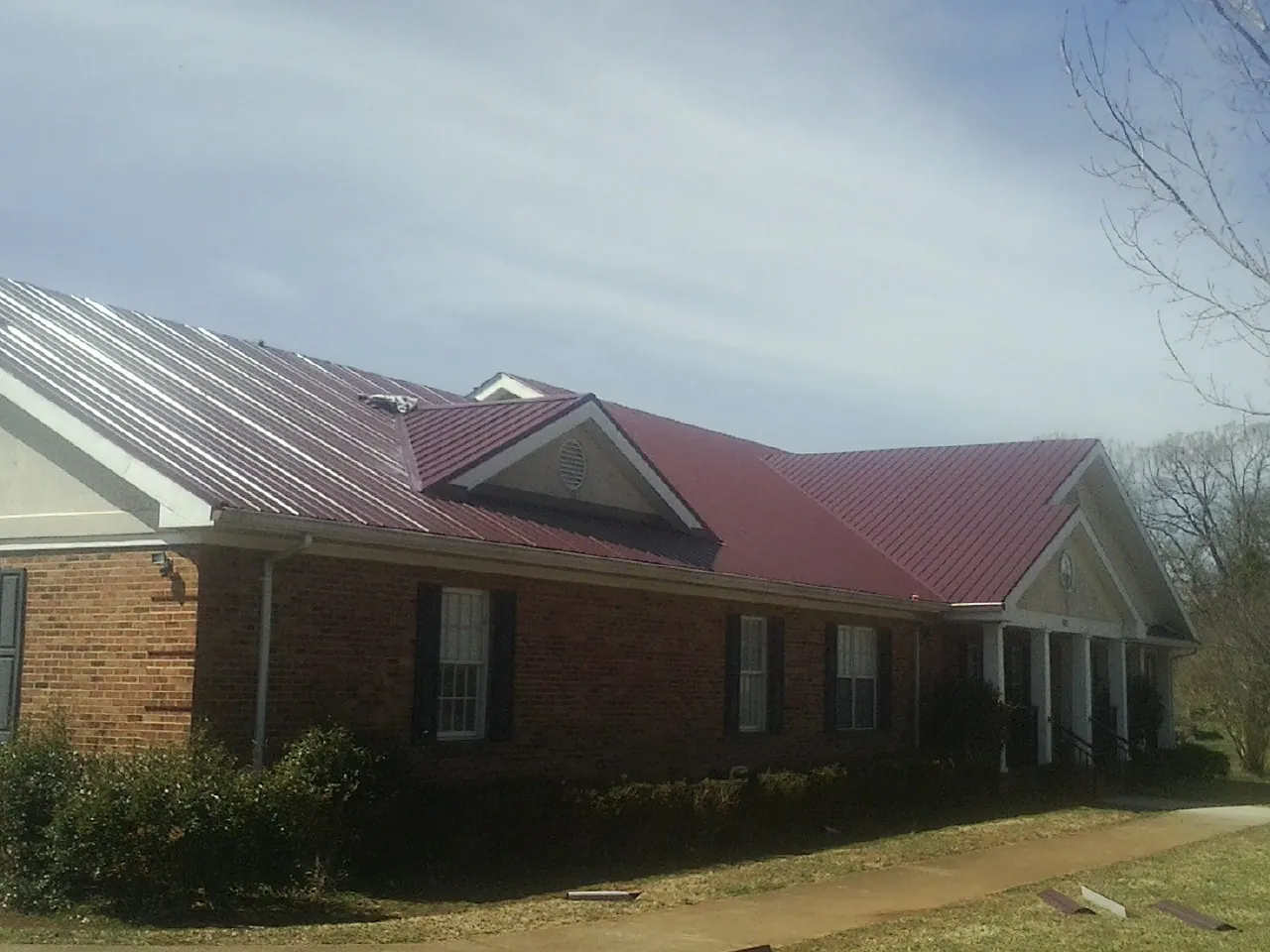 Red metal roof with gabled entries on a long brick building, from a Hail Damage Roof Repair job in Morgan City