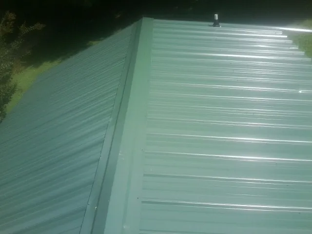 New green metal panels meeting at the ridge of a roof — Flat Roof Repair work by our crew in Morgan City