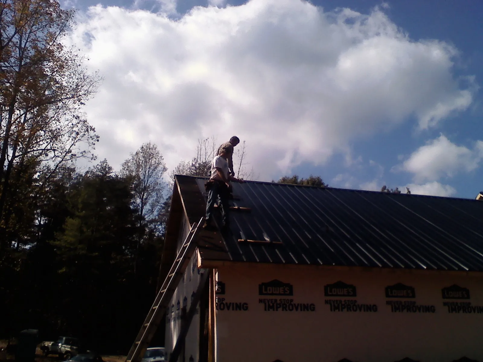 Roofer fastening dark metal panels high against a cloudy sky, from a Roof Inspection job in Morgan City
