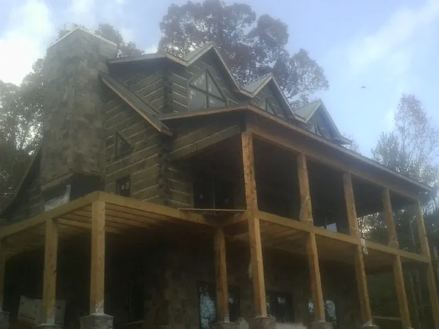 Stone chimney and dormers on a large log home with a timber porch in Morgan City