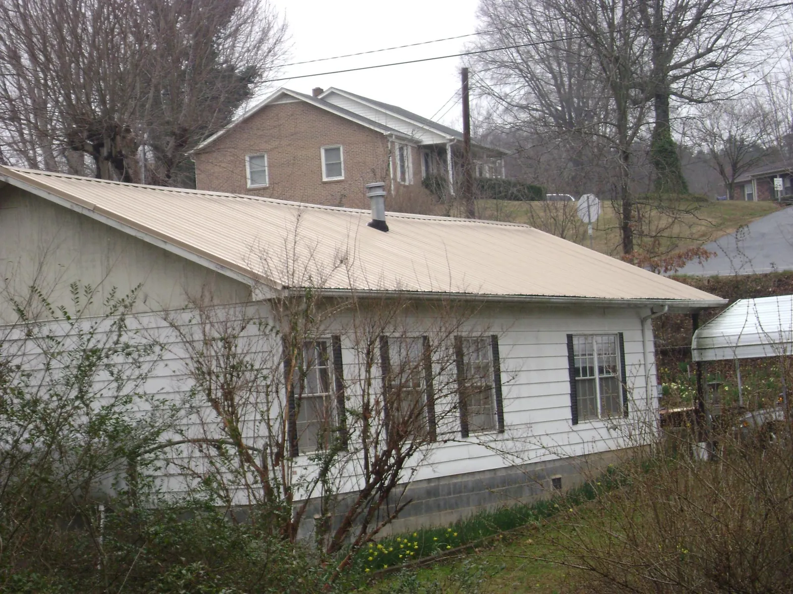 Tan metal roof on a white sided house set into a hillside — Commercial Roofing by Roofing Brothers in Morgan City